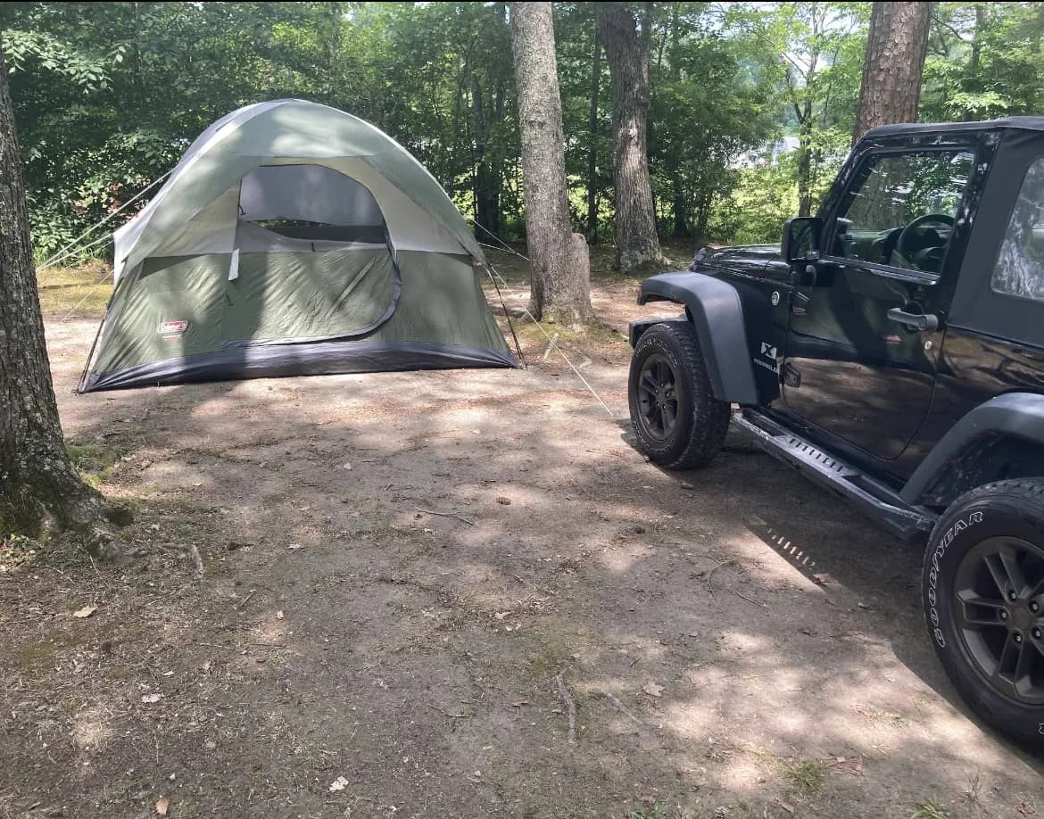 Primitive tent camping site in wooded area with green Coleman tent and Jeep Wrangler